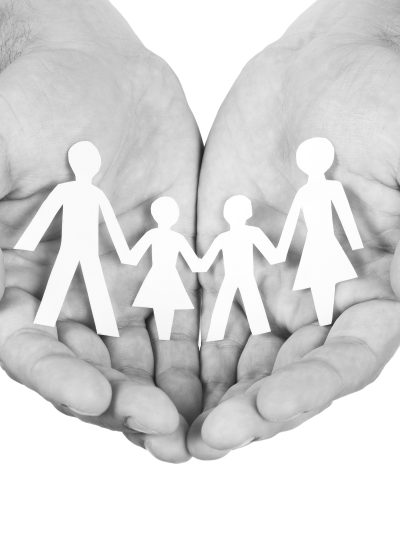 Black and white photo of cupped hands holding a paper cut-out of a family
