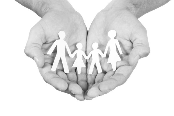 Black and white photo of cupped hands holding a paper cut-out of a family
