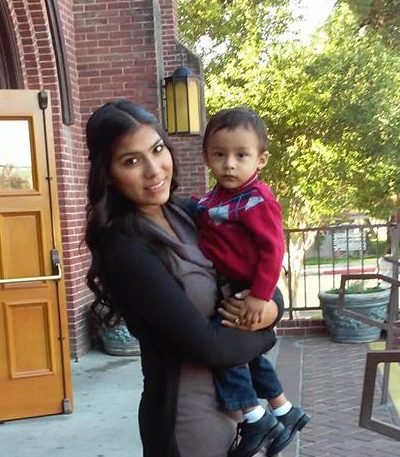 Angelica stands on the steps in front of her school, holding her son Joel