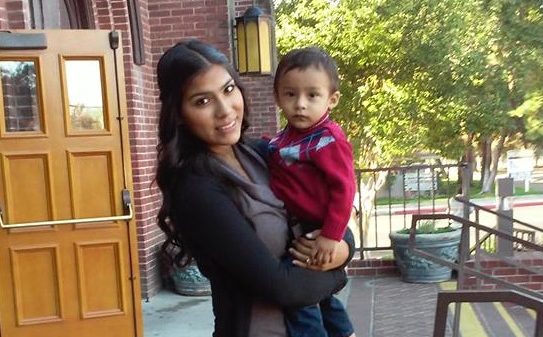Angelica stands on the steps in front of her school, holding her son Joel