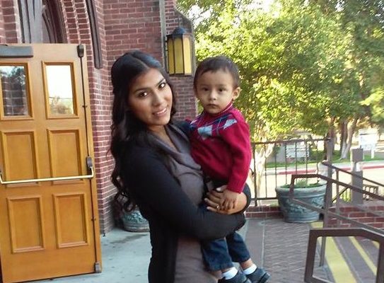 Angelica stands on the steps in front of her school, holding her son Joel
