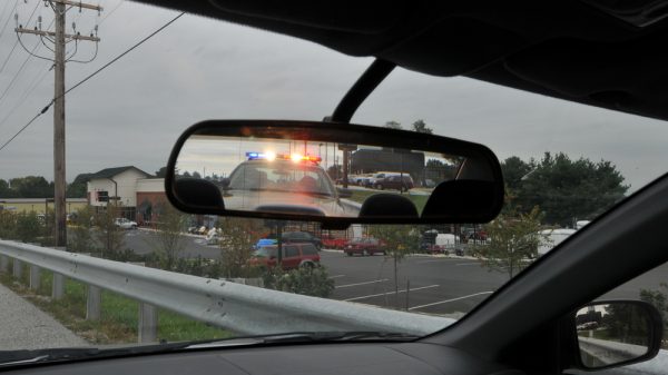 vehicle rear-view mirror showing police cruiser and active lights