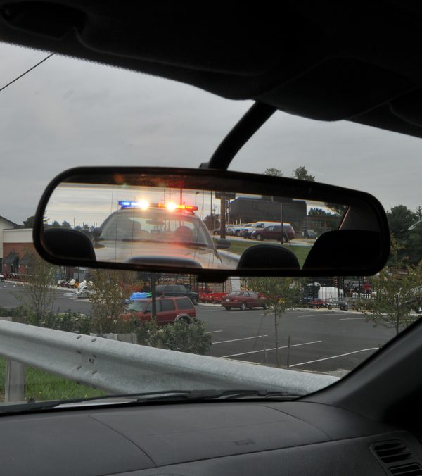 vehicle rear-view mirror showing police cruiser and active lights