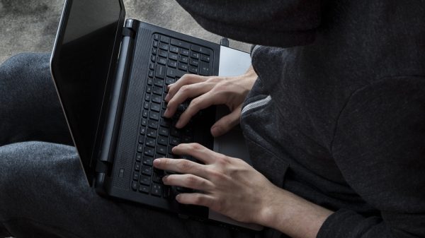 person wearing a hooded sweatshirt typing on laptop
