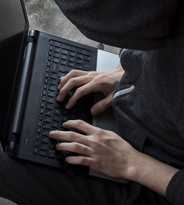 person wearing a hooded sweatshirt typing on laptop