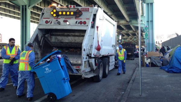 Workers throw homeless people's property into a Caltrans truck