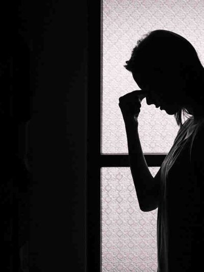 backlit photo of woman holding her forhead in despair