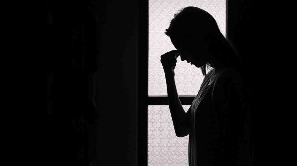 backlit photo of woman holding her forhead in despair
