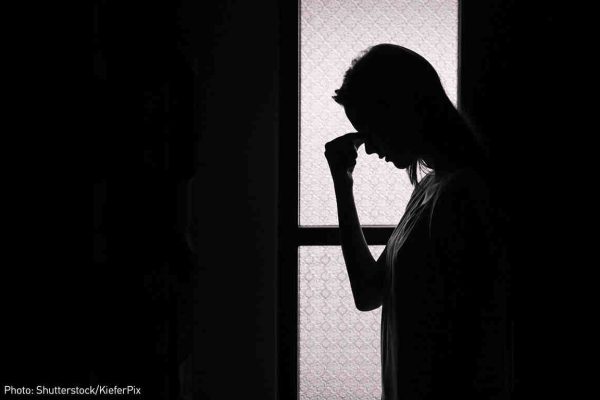 backlit photo of woman holding her forhead in despair