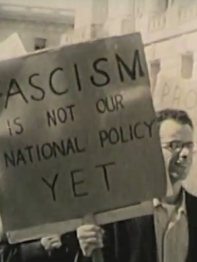 man holds sign saying "Fascism is not our national policy yet"