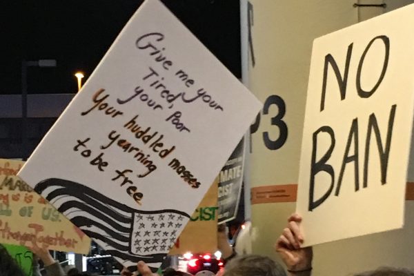 Signs at SFO protest read "No Ban"