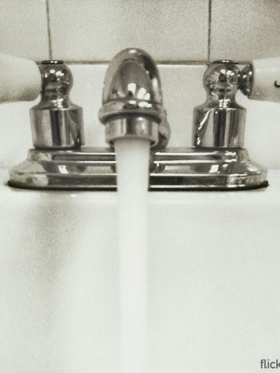 Black and white image of water flowing out of a tap into a porcelain sink