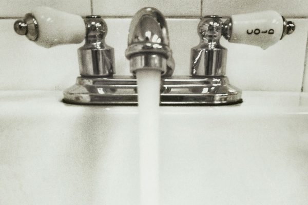 Black and white image of water flowing out of a tap into a porcelain sink