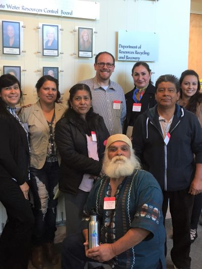 A group of 13 people stands outside the hearing room of the State Water Resources Control Board, ready to provide public comment on the contaminant 1,2,3-TCP