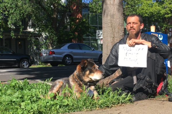 Plaintiff James "Faygo" Clark sits by a Sacramento street corner with a sign and his dog.