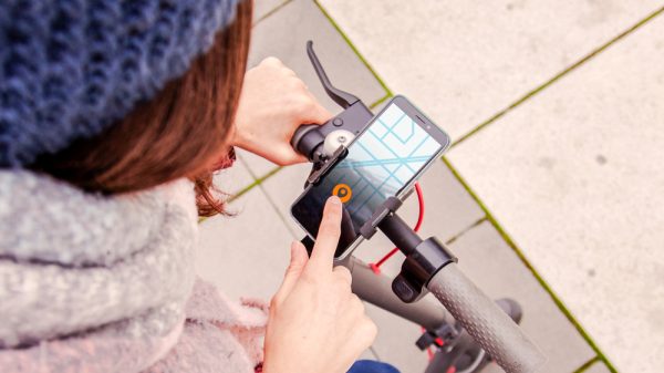 Woman operating mobile application standing atop scooter