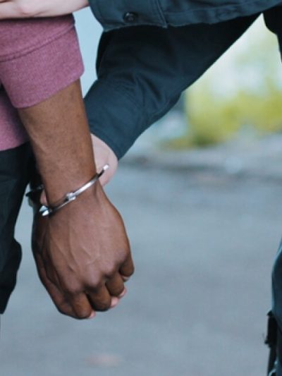 Black man with his hands behind his back and being placed in handcuffs by a uniformed police officer