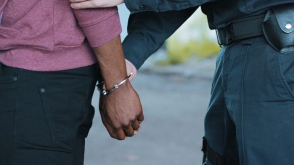 Black man with his hands behind his back and being placed in handcuffs by a uniformed police officer