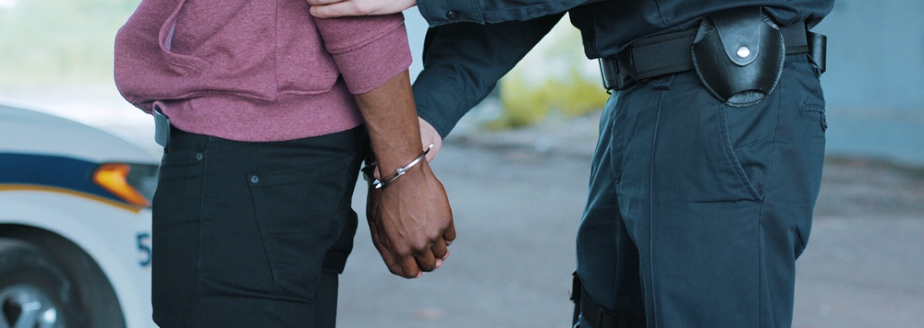 Black man with his hands behind his back and being placed in handcuffs by a uniformed police officer