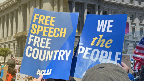 people holding up signs at a protest saying "Free speech free country" and "We the people"