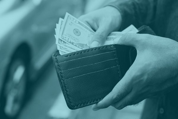 A person holding open a wallet and thumbing through U.S. dollars.