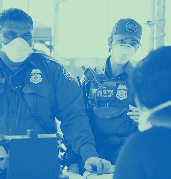 Customs and Border Patrol officer questioning a person at a port of entry. Both are wearing face masks.