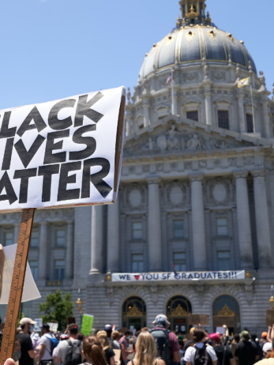 a person is holding a sign that says Black Lives Matter in front of the San Francisco City Hall building