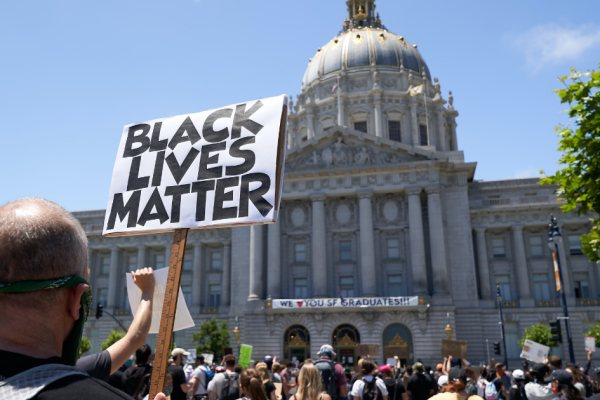 a person is holding a sign that says Black Lives Matter in front of the San Francisco City Hall building