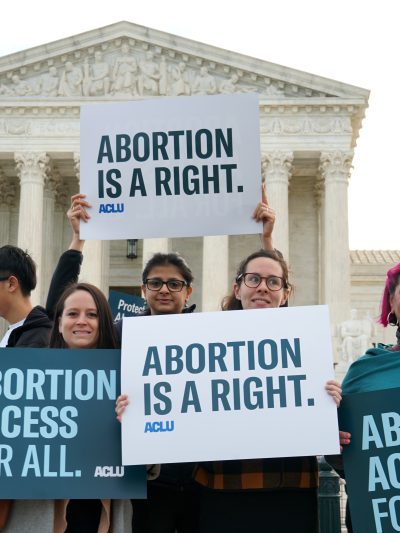 Four people holding signs outside of the Supreme Court that read "Abortion is a right" and "Abortion access for all"