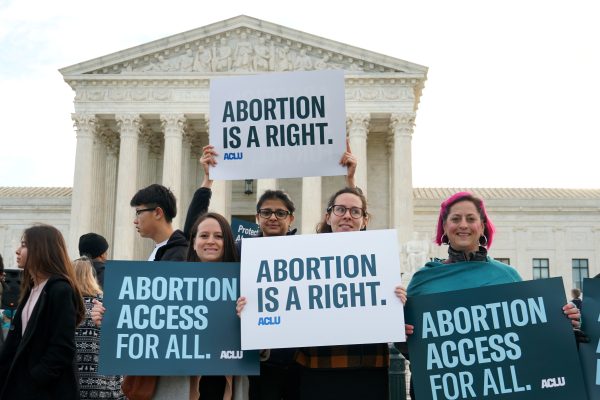 Four people holding signs outside of the Supreme Court that read "Abortion is a right" and "Abortion access for all"