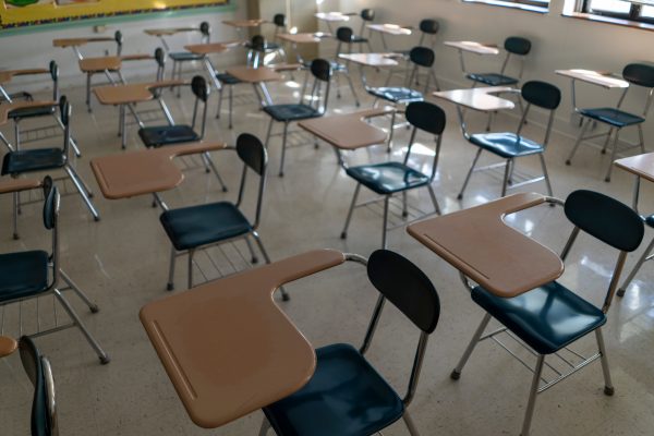 Desks in empty dark high, middle, or elementary school classroom with light coming through windows.