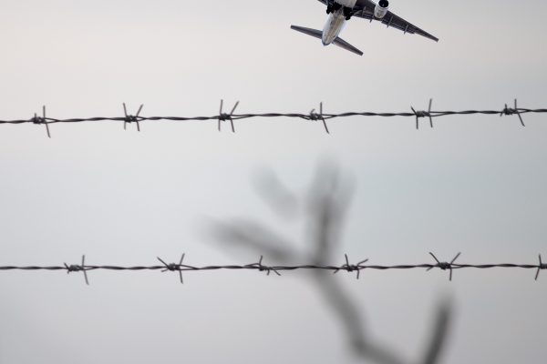 plane flying with barbed wire fence in foreground