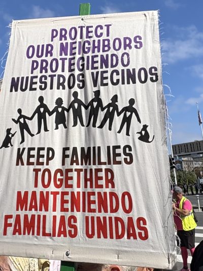 Protest sign reading "Protect our neighbors, keep families together" in English and Spanish