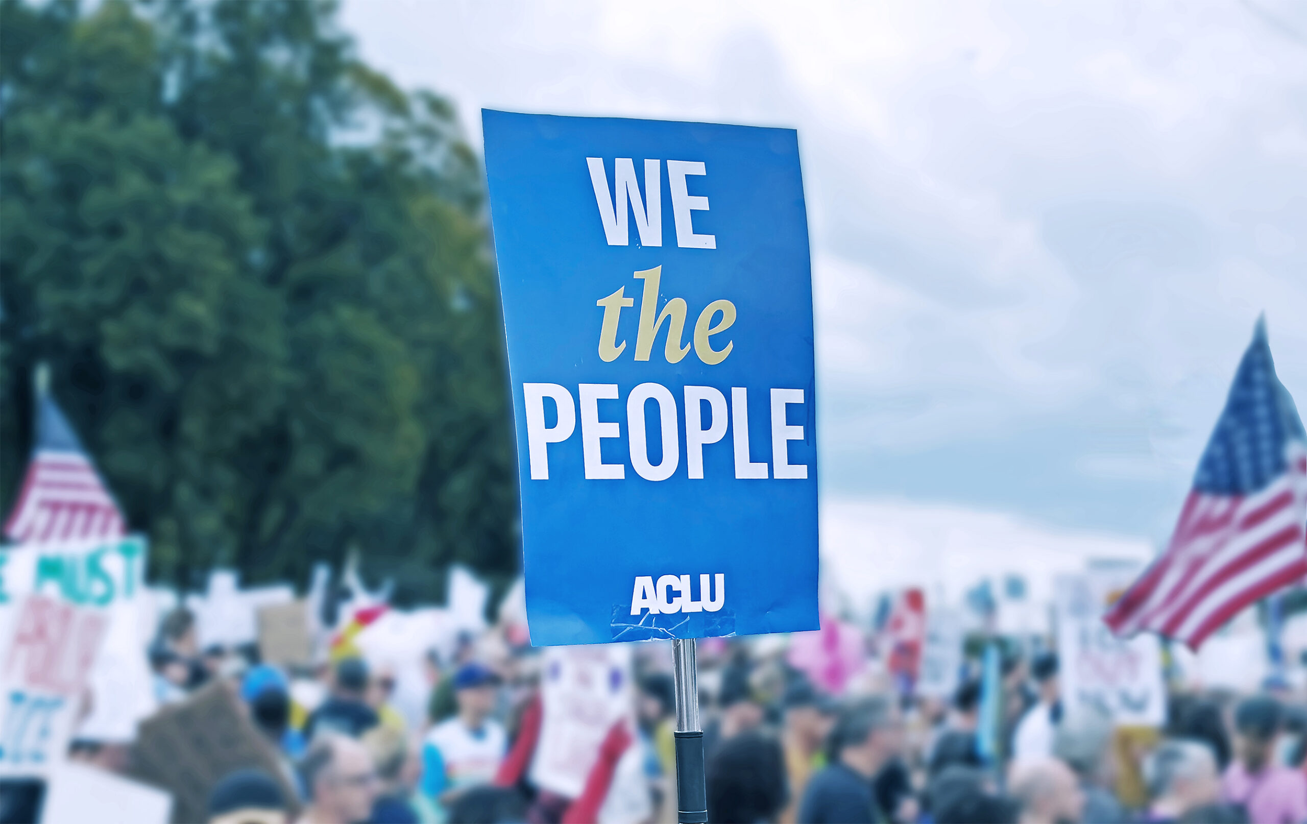 An ACLU "We the People" sign amidst an outdoor rally