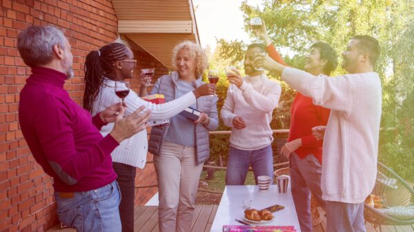 A group of individuals gathered around an outdoor table, smiling and raising their glasses to each other