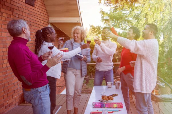 A group of individuals gathered around an outdoor table, smiling and raising their glasses to each other