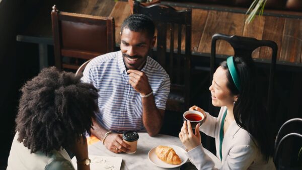 Three people sit around a small table having coffee together