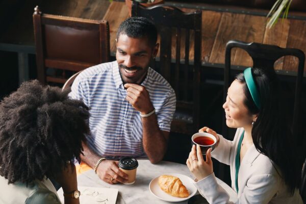 Three people sit around a small table having coffee together