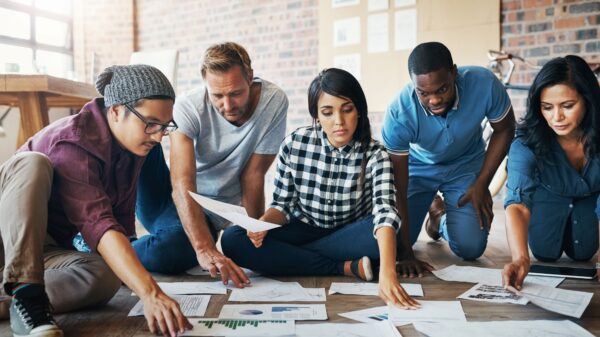 Co-workers sitting on the floor together reviewing various papers and work