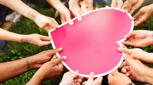 Many hands holding a large cutout pink heart