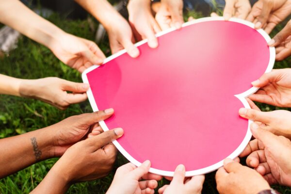 Many hands holding a large cutout pink heart