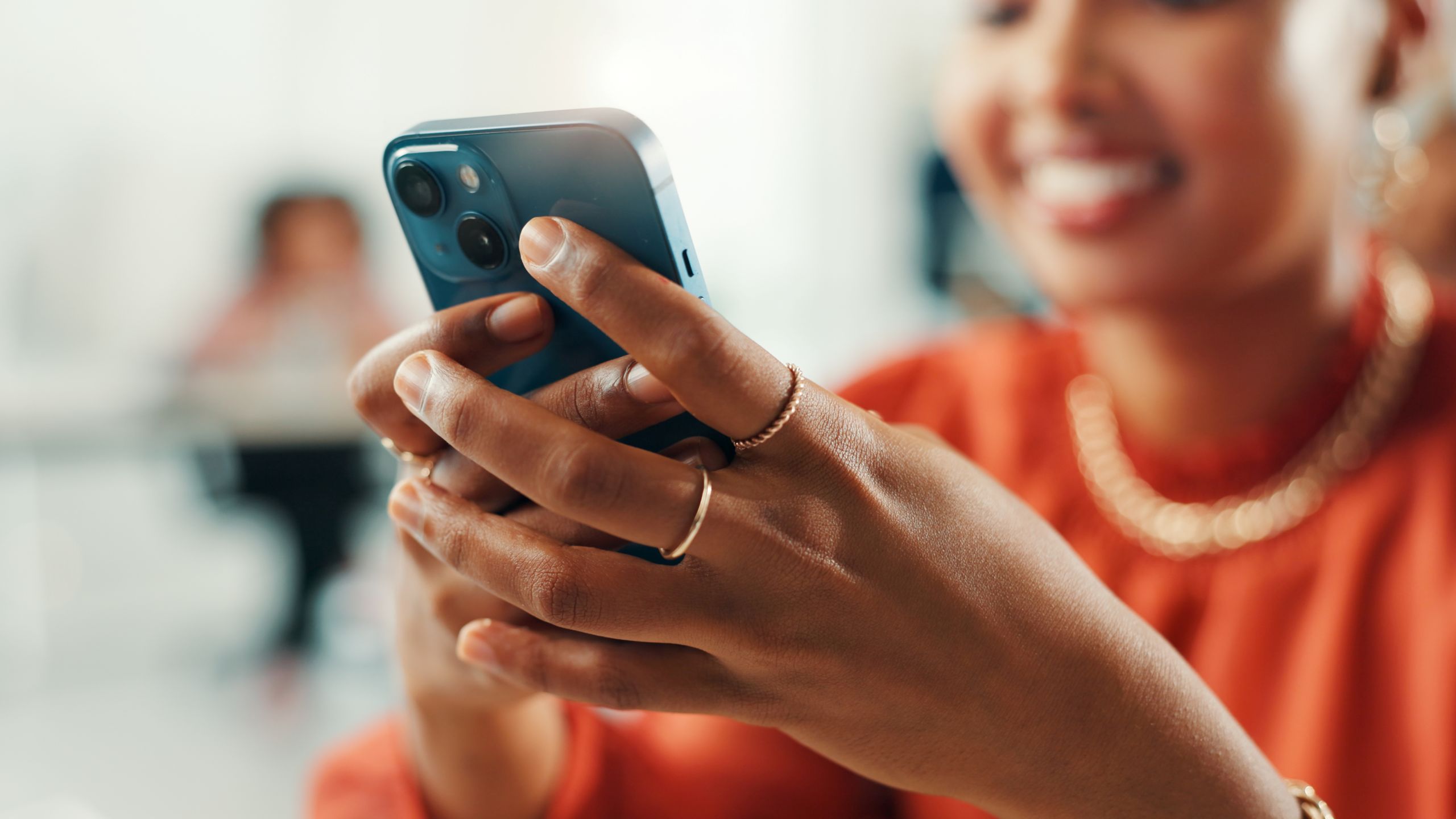 Young Black woman in an orange shirt smiling while looking at her phone.