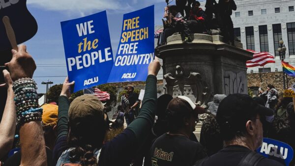 Photo of a people at a protest holding up ACLU branded signs saying, 'We the People' and 'Free Speech, Free Country.'