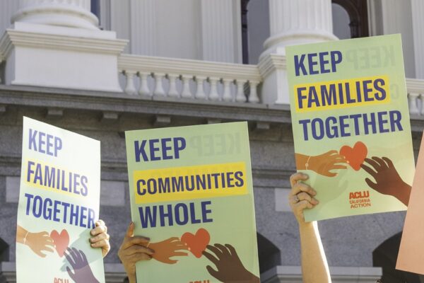 people at the CA state capitol holding signs that say "keep communities whole" and "keep families together"