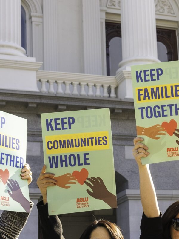 people at the CA state capitol holding signs that say "keep communities whole" and "keep families together"
