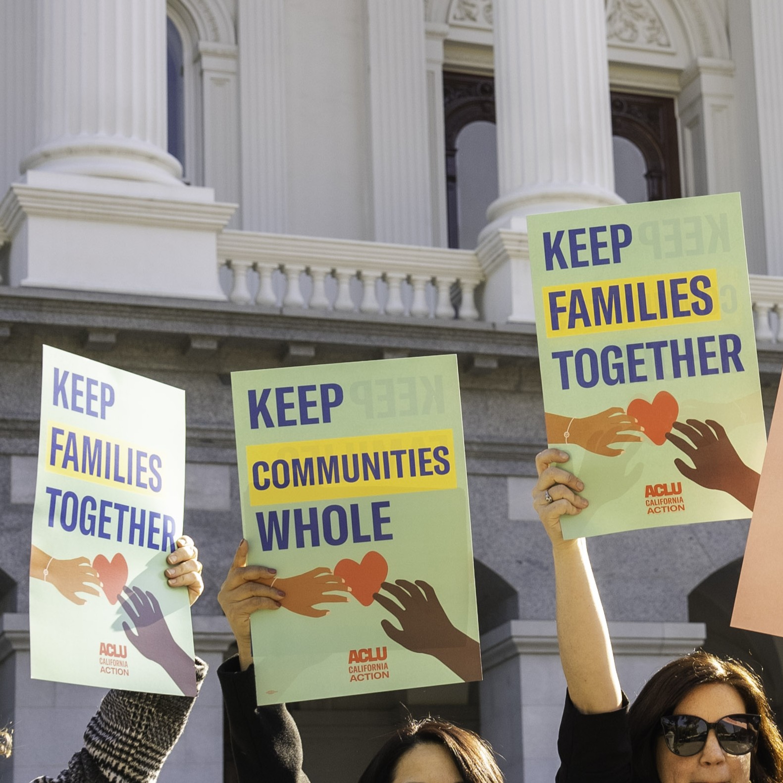 people at the CA state capitol holding signs that say "keep communities whole" and "keep families together"