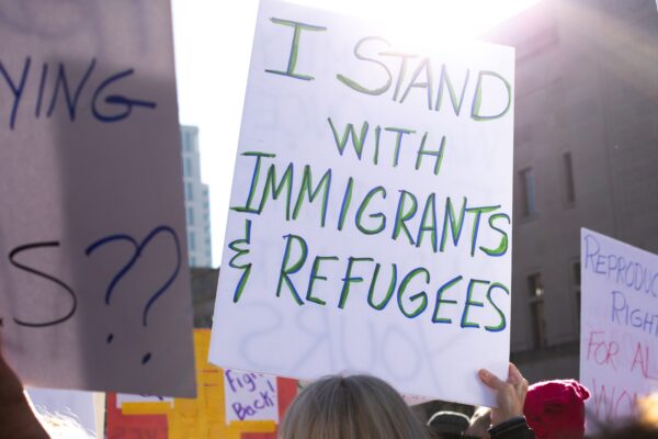 Rally crowd with sign saying "I stand with immigrants and refugees"