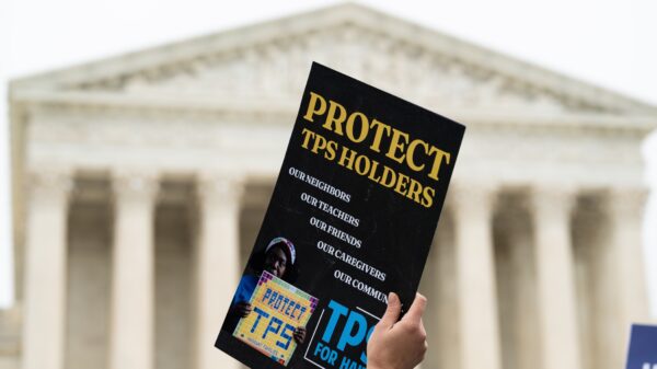 Hand holding a sign that says "Protect TPS holders" in front of the U.S. Supreme Court