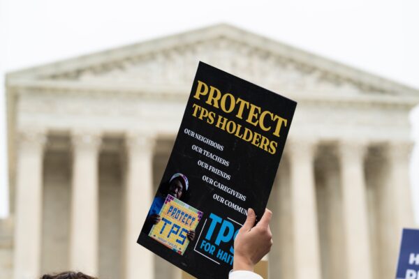 Hand holding a sign that says "Protect TPS holders" in front of the U.S. Supreme Court
