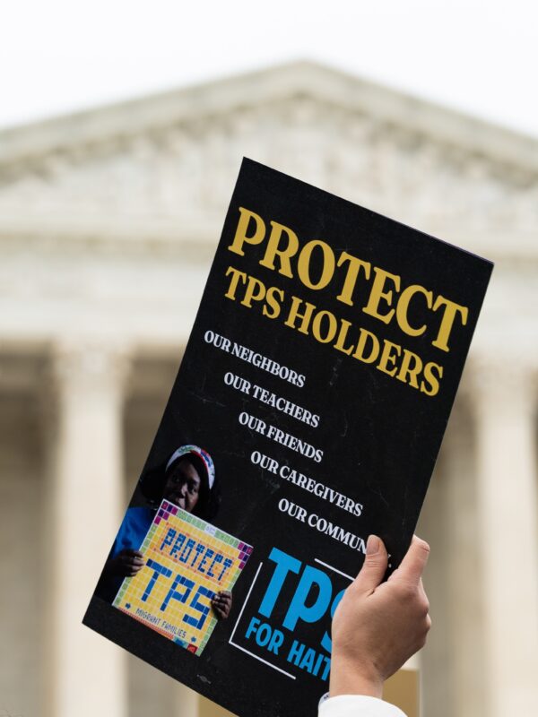 Hand holding a sign that says "Protect TPS holders" in front of the U.S. Supreme Court